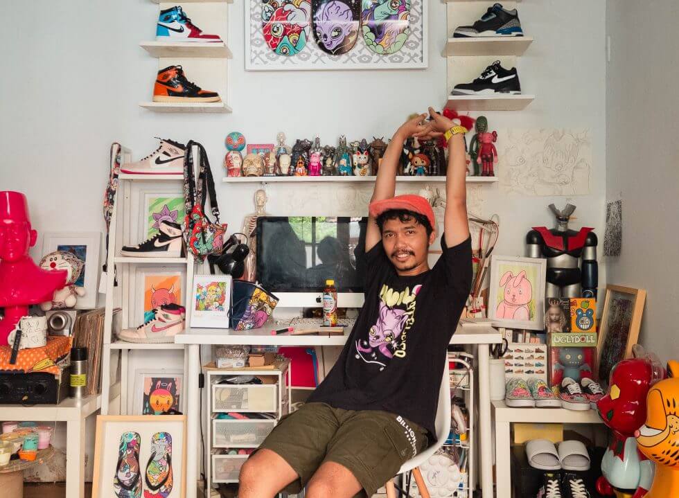 Muklay sedang duduk di dalam studionya, terlihat koleksi sneakers